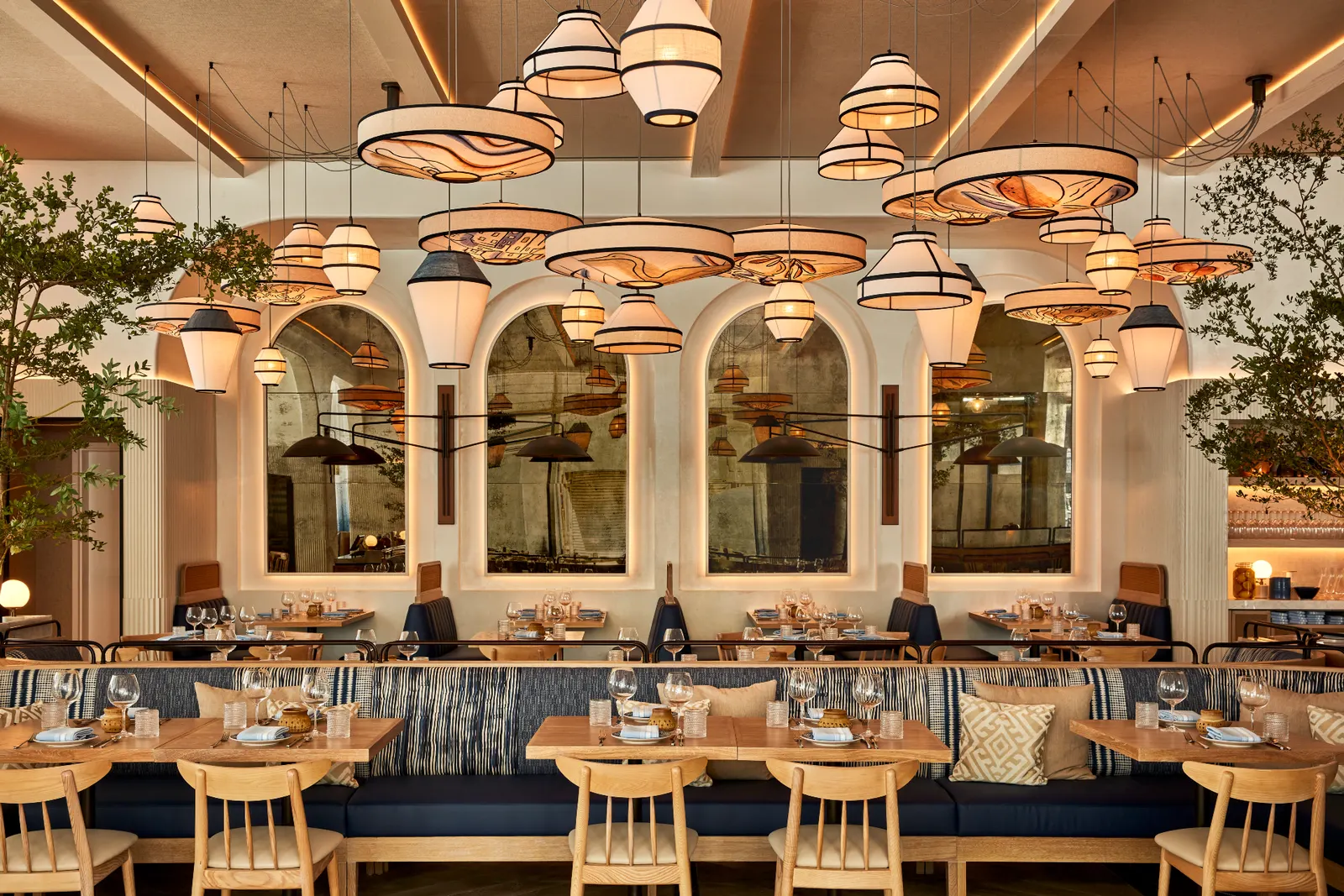 Brasserie with long upholstered banquettes, timber tables and woven pendant lamps