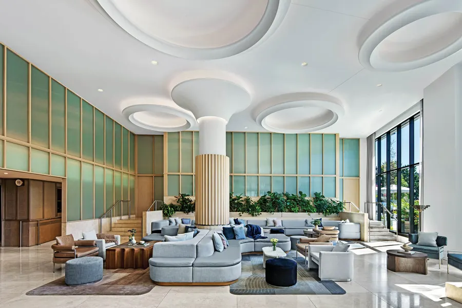 Bright hotel lobby lounge with green glazed panels, sculpted ceiling discs and low sofas
