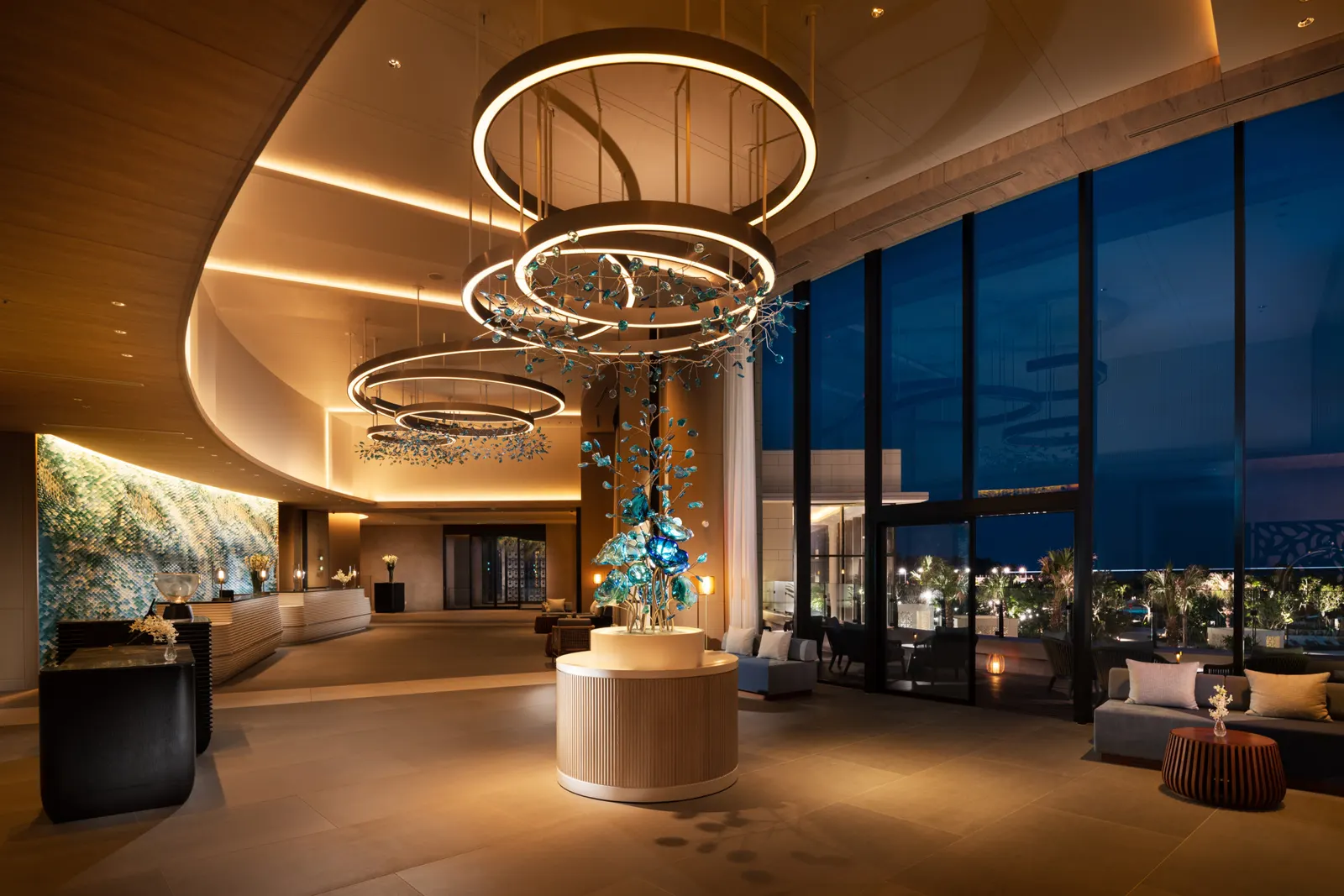 Hotel lobby with layered ring chandeliers, curved timber ceiling and a round reception island
