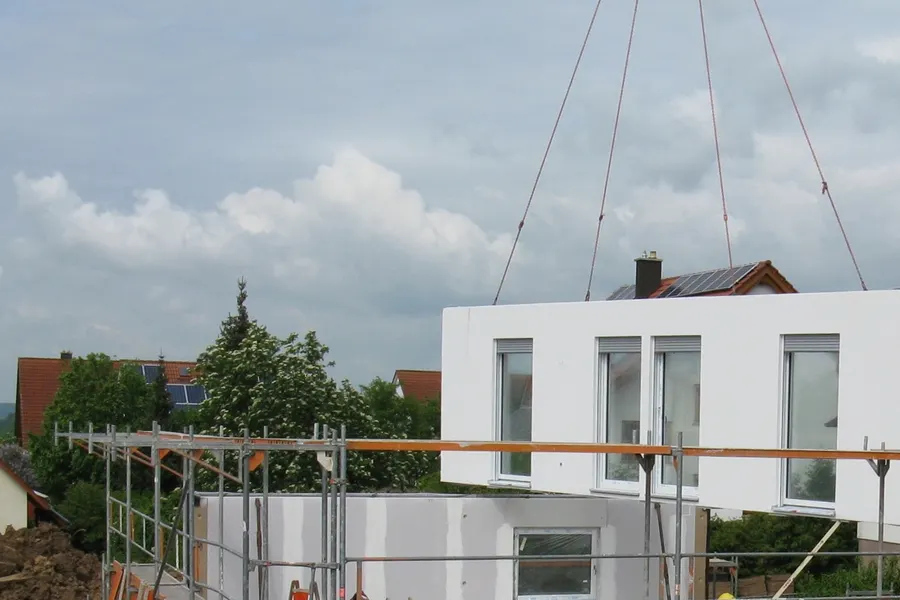 A prefabricated building module lifted by crane onto a small building site