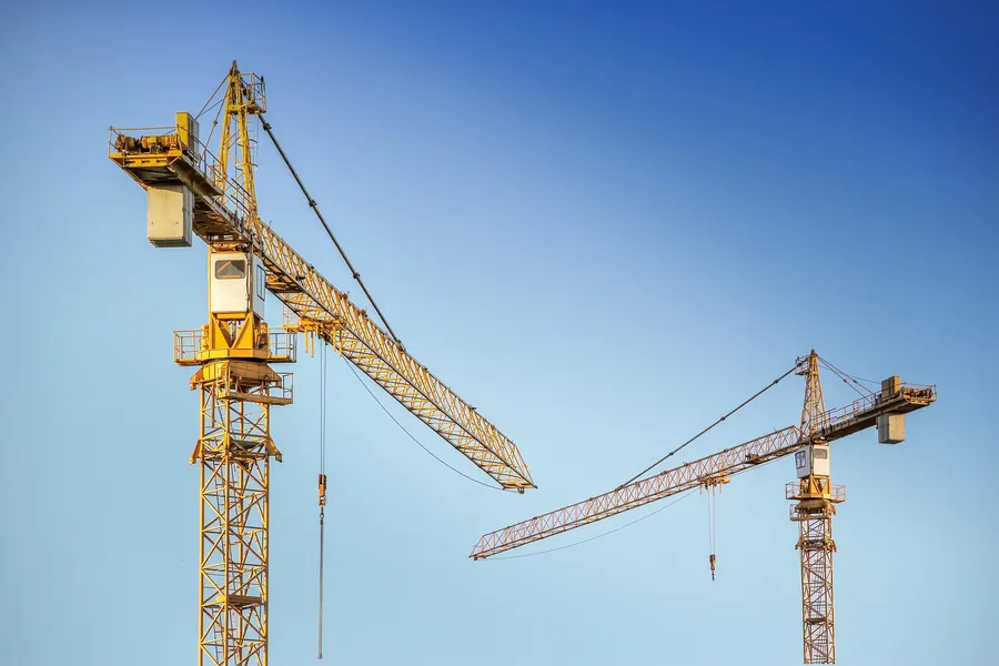 Two tower cranes against a clear blue sky