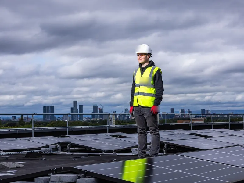 Person in a hard hat and high-visibility vest standing on a flat roof with solar panels