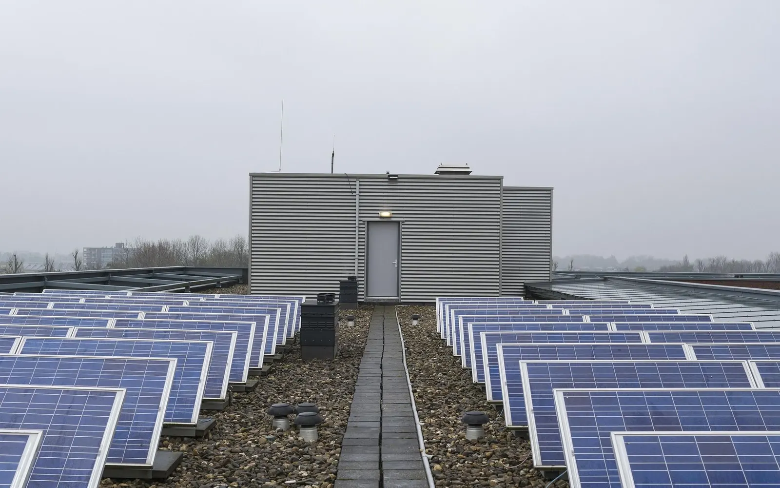 Rows of solar panels on a flat commercial roof leading to a rooftop plant room