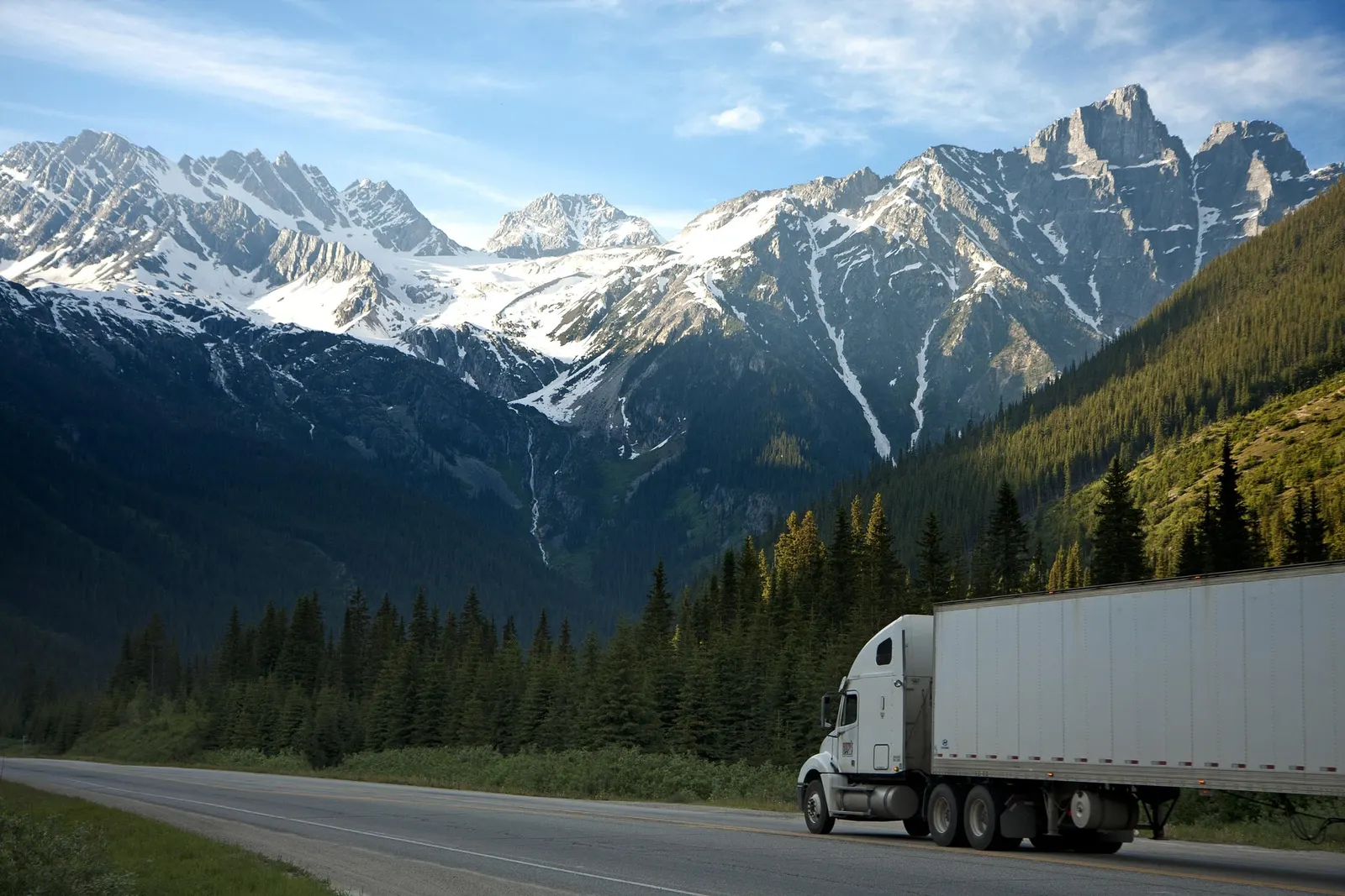 Articulated lorry on a mountain highway with snow-capped peaks behind